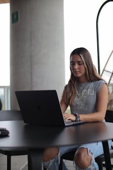 A young woman using a laptop at a desk, focused on online learning indoors.