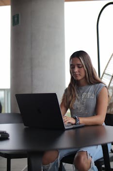Teen girl focusing on online learning using a laptop in a modern indoor setting.