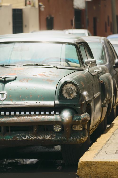 Free A retro car with a rusty exterior parked on a city street, exuding vintage charm. Stock Photo