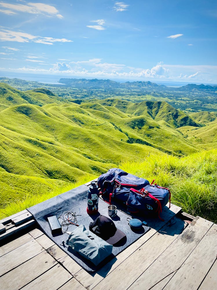 Hiking Equipment On Wooden Platform Over Green Hills