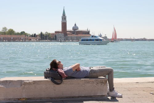 A Man Lying on a Bench near the Water with View of the San Giorgio Maggiore Church in the Background in Venice, Italy 