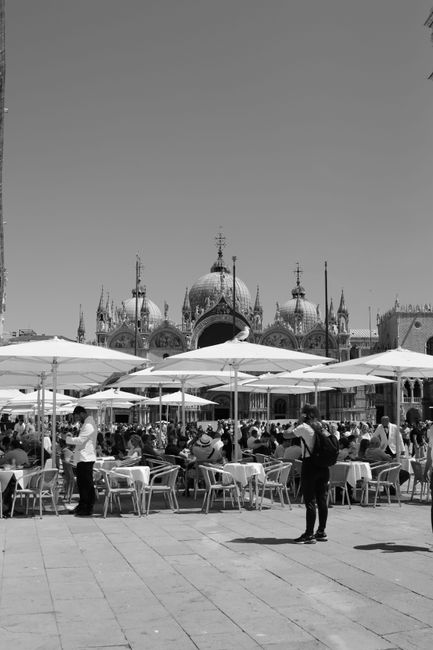 Black and white photograph of Piazza San Marco in Venice with people dining outdoors.