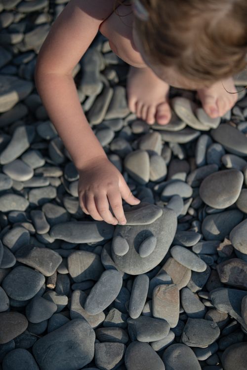 Free Top view of a child arranging pebbles on a beach, creating fun shapes under the sunlight. Stock Photo