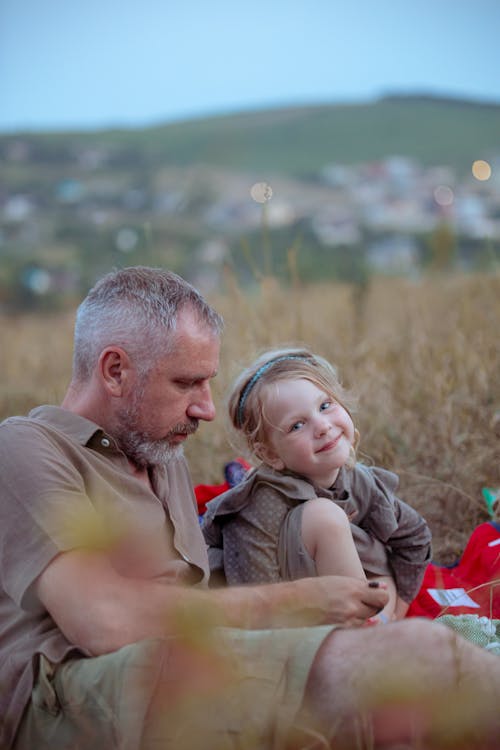Father and Daughter Sitting Together on a Grass Field 