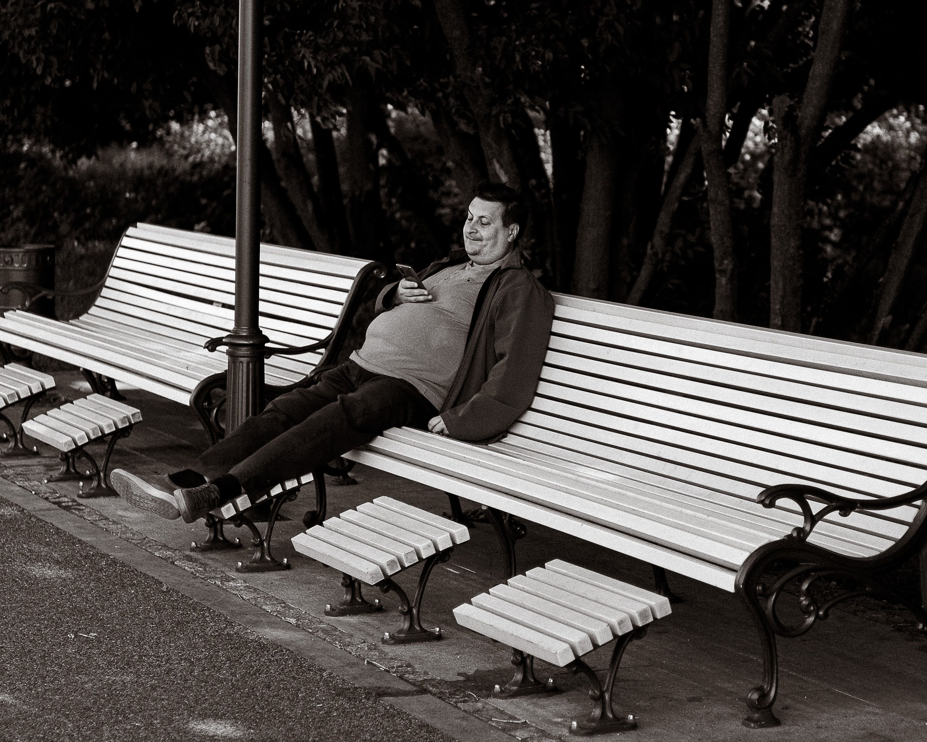 A person sitting alone on a park bench, smiling while looking at their phone