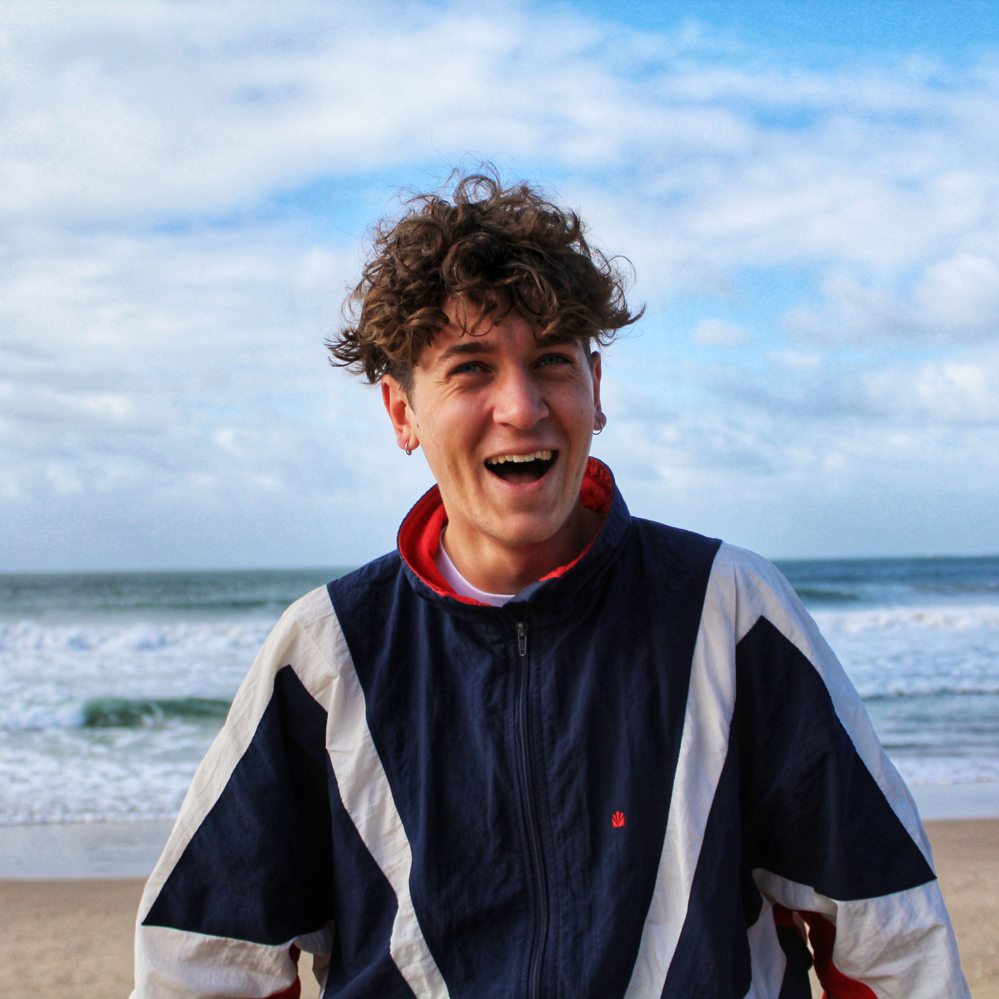 Laughing young man in sports jacket at the beach on a bright day.