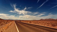 在充满活力的蓝天和缕缕云层下，长长的沙漠高速公路一直延伸到地平线