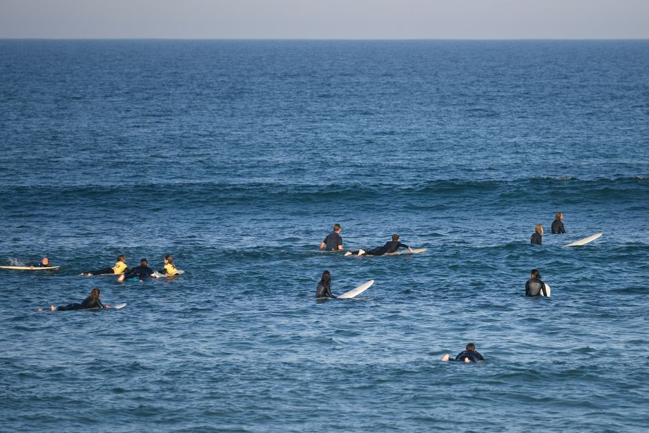 A group of surfers in wetsuits waiting for waves on a sunny day at sea.