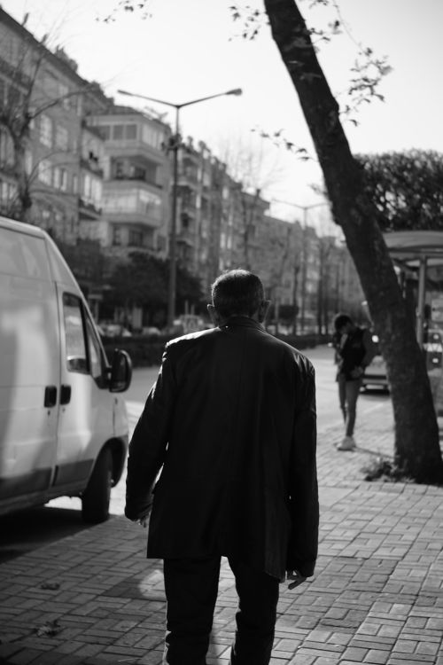Free A black and white photo of an elderly man walking on a city sidewalk, capturing urban life. Stock Photo