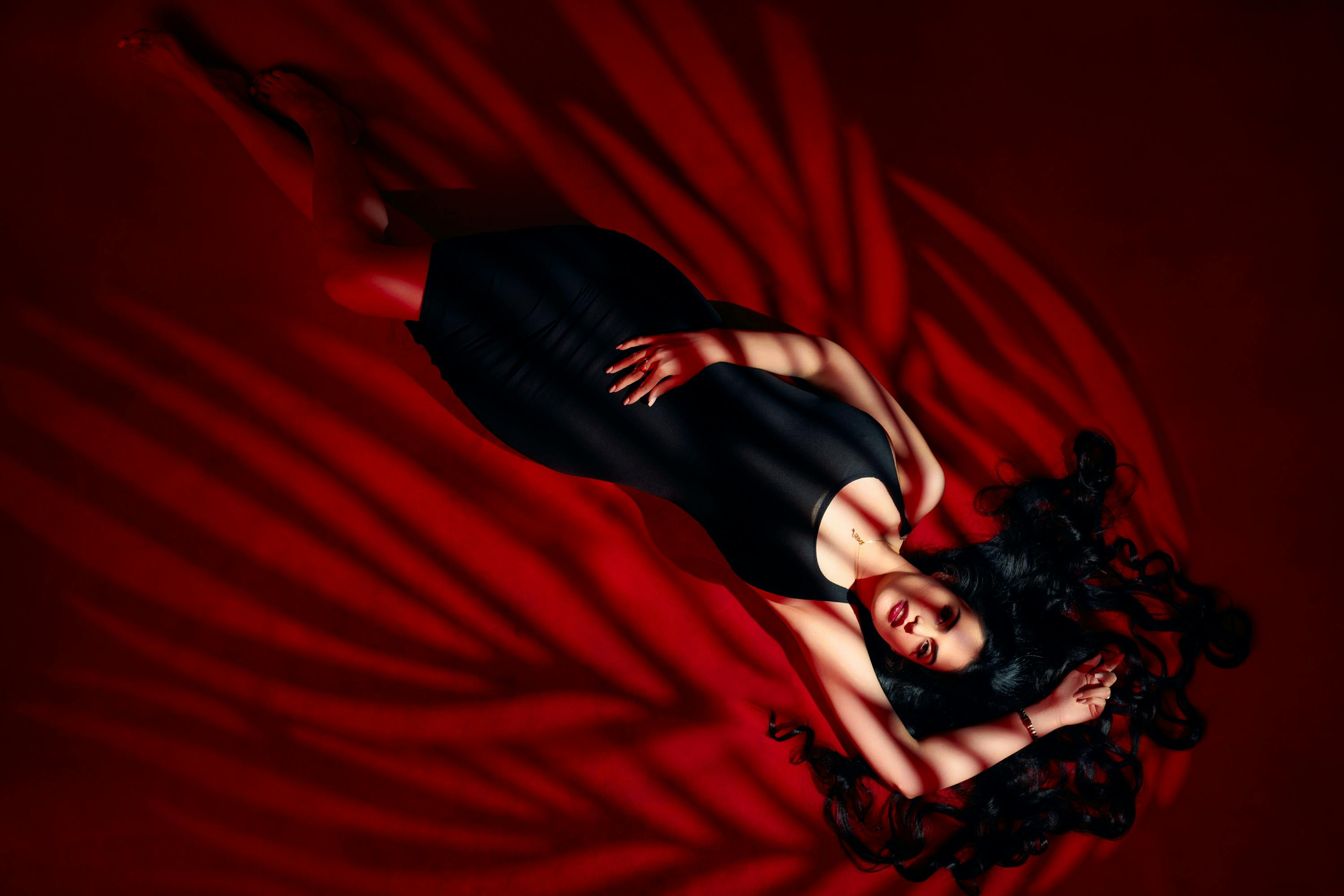 Stylish brunette woman in a black dress posing elegantly with striking red lighting.