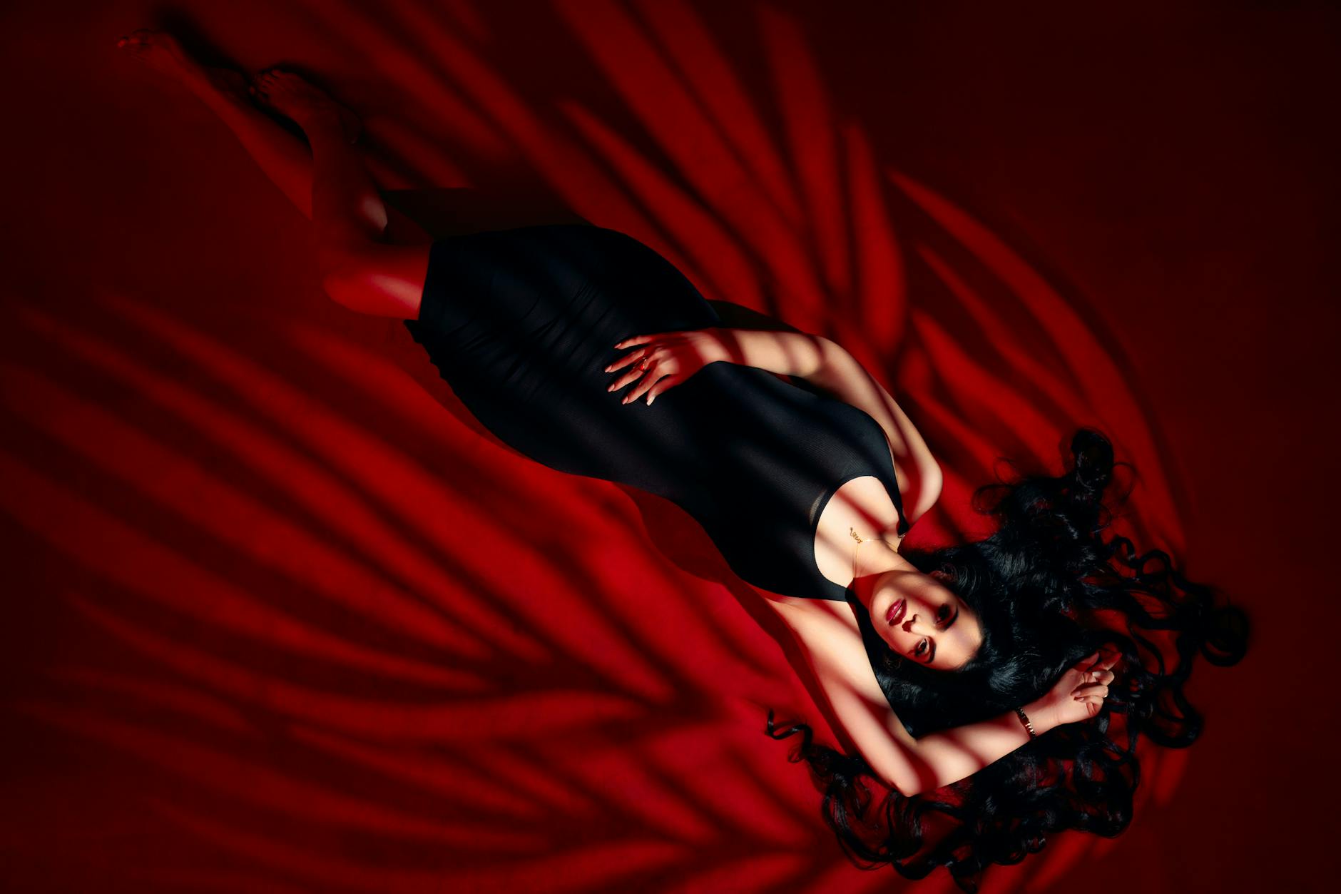 Stylish brunette woman in a black dress posing elegantly with striking red lighting.