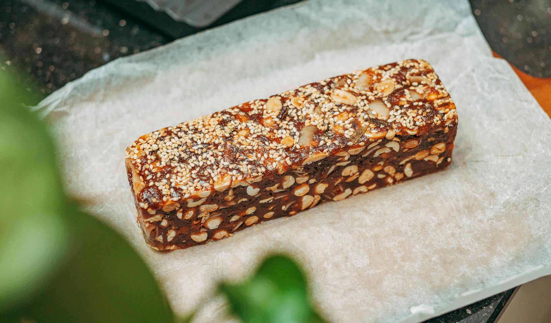 Close-up image of a nut and sesame seed protein bar on parchment paper, ideal for healthy snacking.