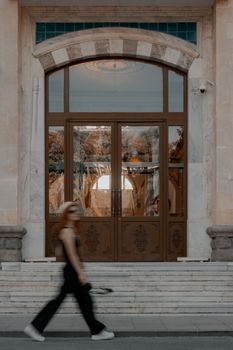 A woman walks past elegant wooden doors with arched windows and detailed architecture.