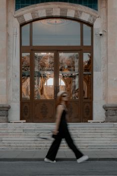Blurred woman walks past a grand building entrance with reflective glass doors, showcasing motion and elegance.