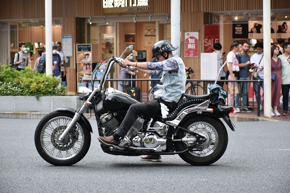 A man rides a stylish black motorcycle on a bustling city street, capturing urban life.