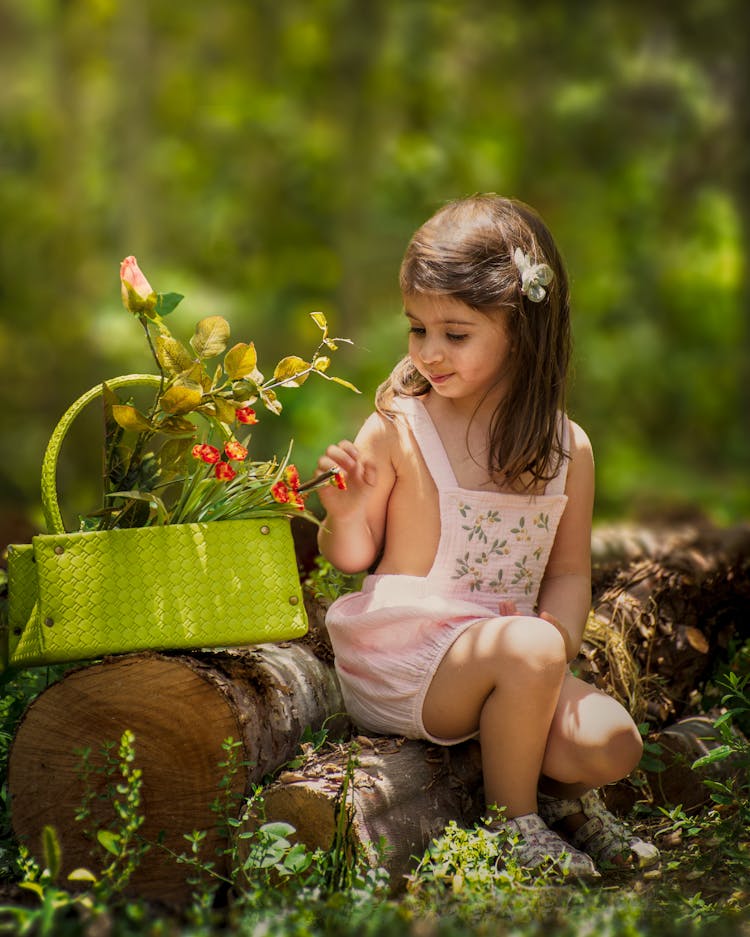 A Little Girl Sitting In The Forest With A Basket Of Flowers