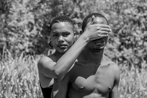 Free Black and white photo of a woman covering a man's eyes, both topless, outdoors. Stock Photo
