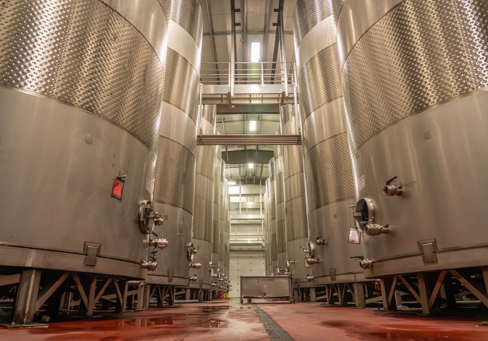 Row of tall stainless steel fermentation tanks with insulated pipework running between them.