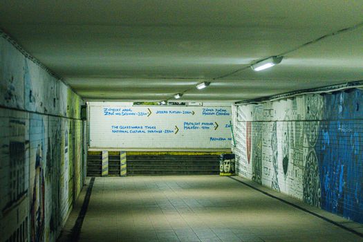 A well-lit underground pedestrian tunnel adorned with graffiti and informative signage.