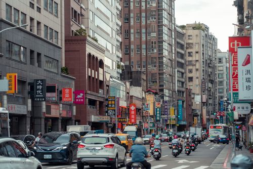 Free Busy downtown street scene in Taiwan with cars and scooters amidst skyscrapers. Stock Photo