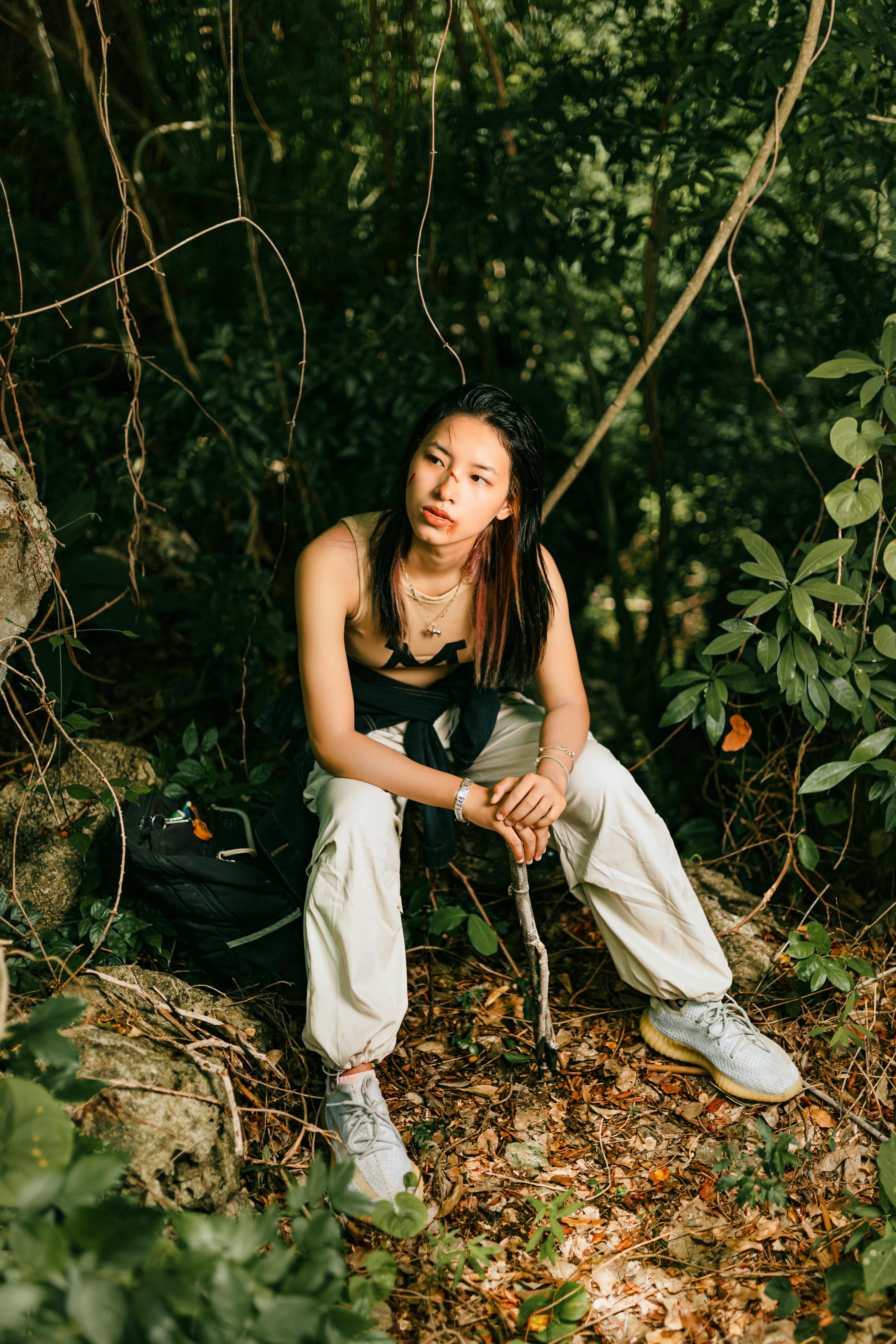 Woman in White Pants with Wounds on Face Sitting by Tree in Forest · Free  Stock Photo