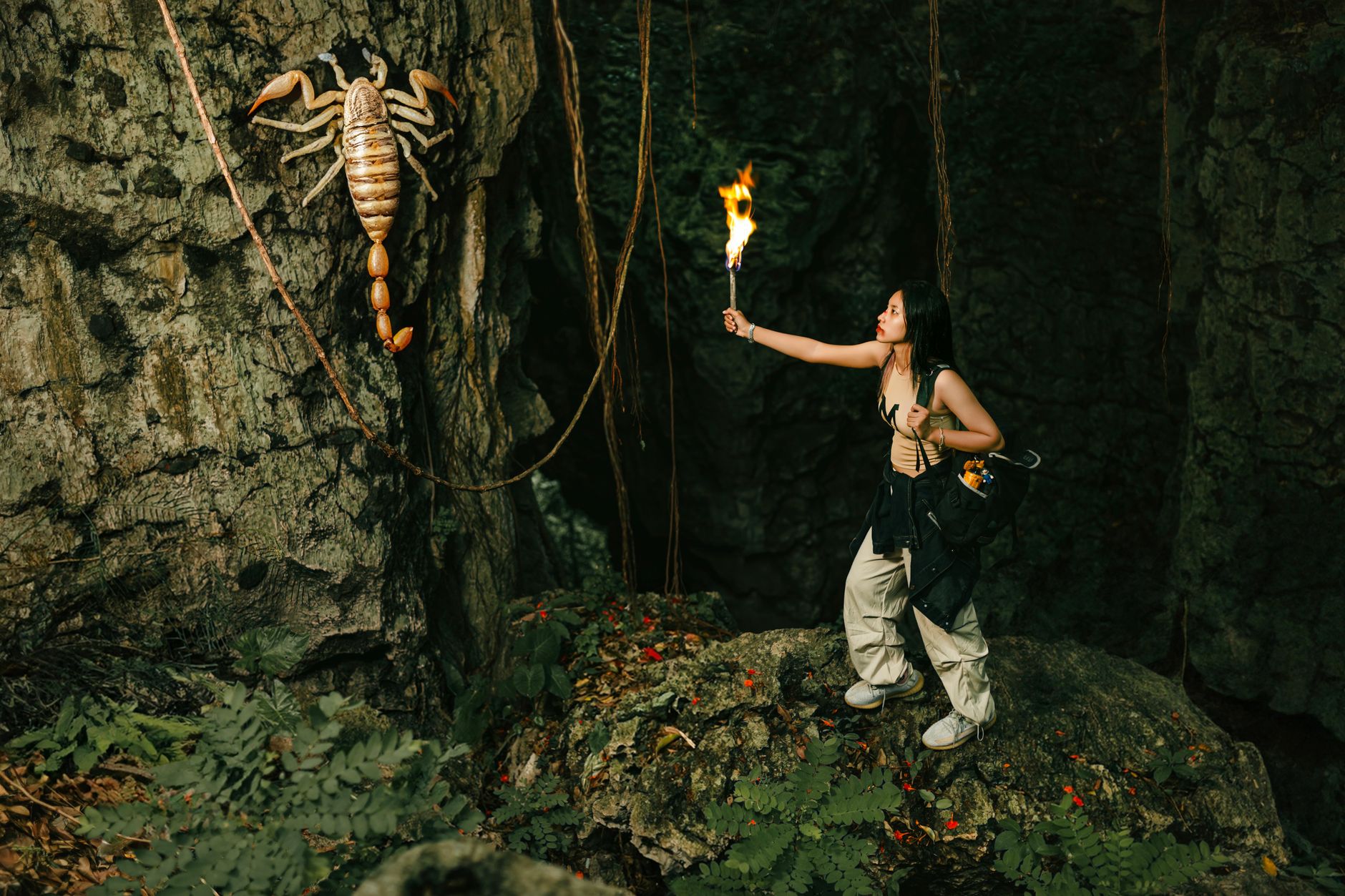 An adventurous woman explores a cave, wielding a torch against a giant scorpion.