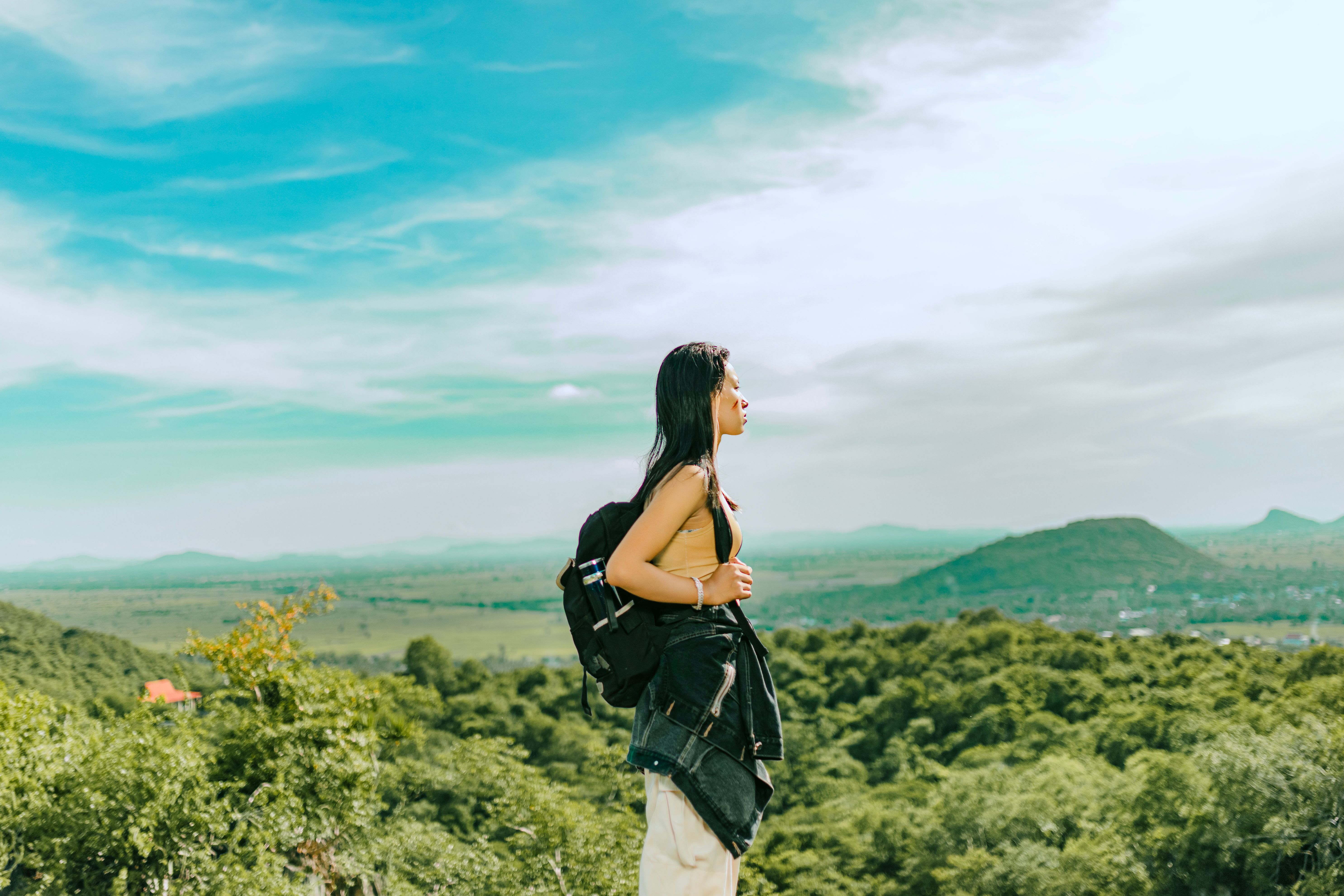 A young Asian woman with a backpack enjoys the freedom and beauty of a lush green forest landscape.