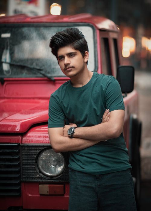 Free Stylish young man with a mustache leaning against a red SUV in an urban setting. Stock Photo