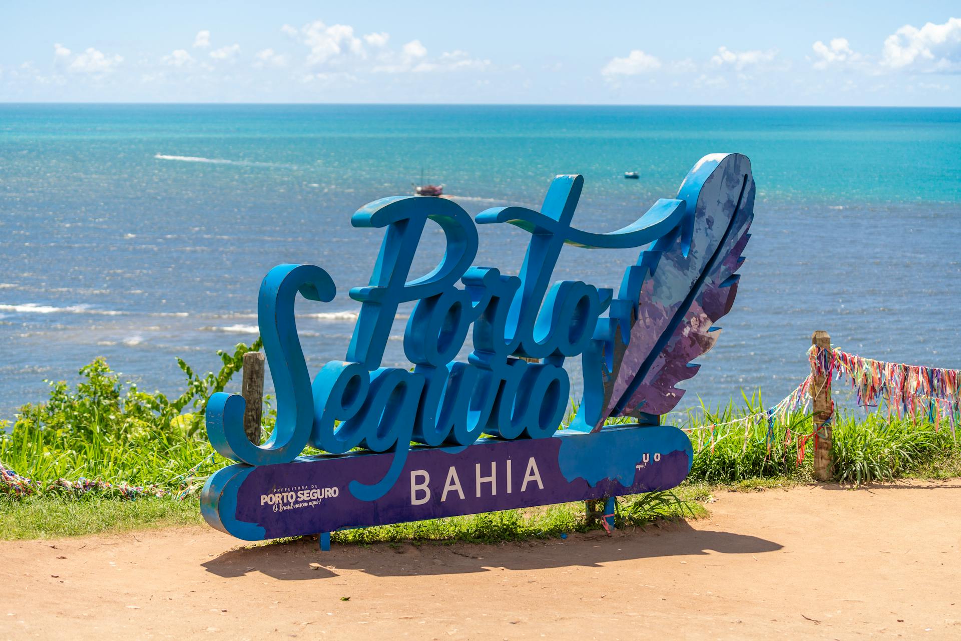 Vibrant Porto Seguro Bahia sign under a sunny blue sky with ocean view.