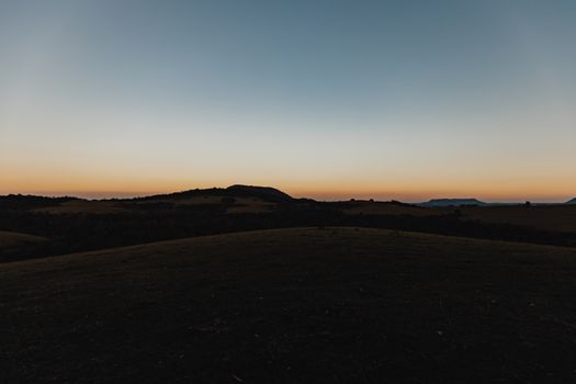 A serene view of a rural landscape at sunset with rolling hills silhouetted against the evening sky.