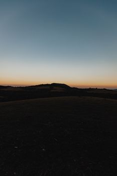 A peaceful rural landscape with hills silhouetted at sunset, showcasing a tranquil meadow.