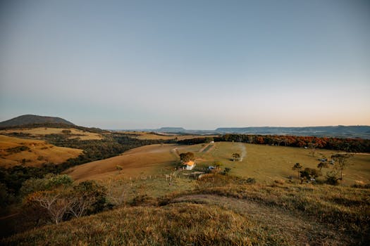 Beautiful panoramic view of a serene rural landscape in Brazil during dusk, featuring hills, meadows, and a farmhouse.