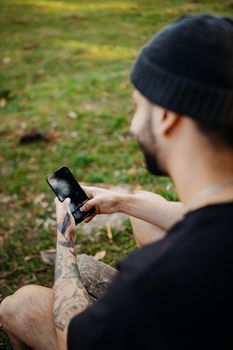 Man with tattoos using smartphone outside in a relaxed setting.