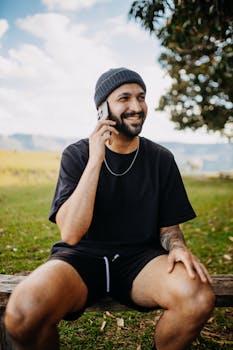Smiling man in casual wear enjoys a phone call outdoors on a sunny day.