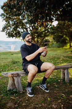 Casual man sitting on a rustic bench using smartphone and enjoying nature.