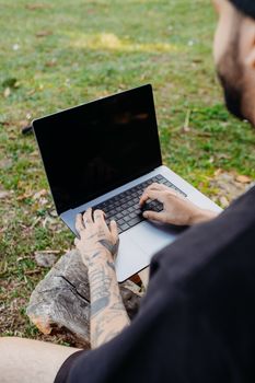 Tattooed man using a laptop while sitting outside on a sunny day.
