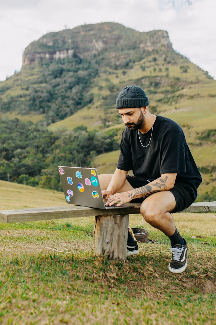 Man Sitting With Laptop On Meadow Against Rocky Mountain