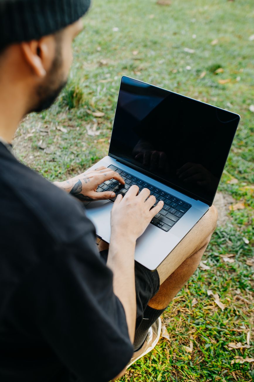 Man using laptop outdoors on grass, focused on work during a sunny day in nature.