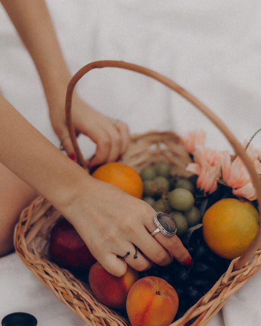 A wicker basket filled with fresh fruits and flowers in a relaxing outdoor picnic setting.