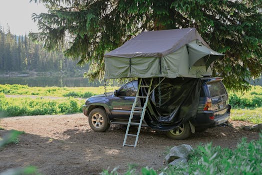 A car equipped with a rooftop tent is parked in a serene forest campsite by the lake.