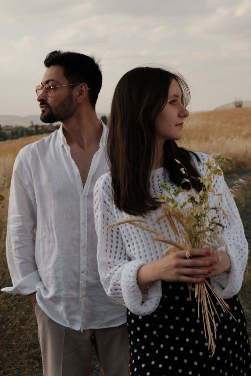 Free Stylish couple standing in a golden field, holding wildflowers during twilight. Stock Photo