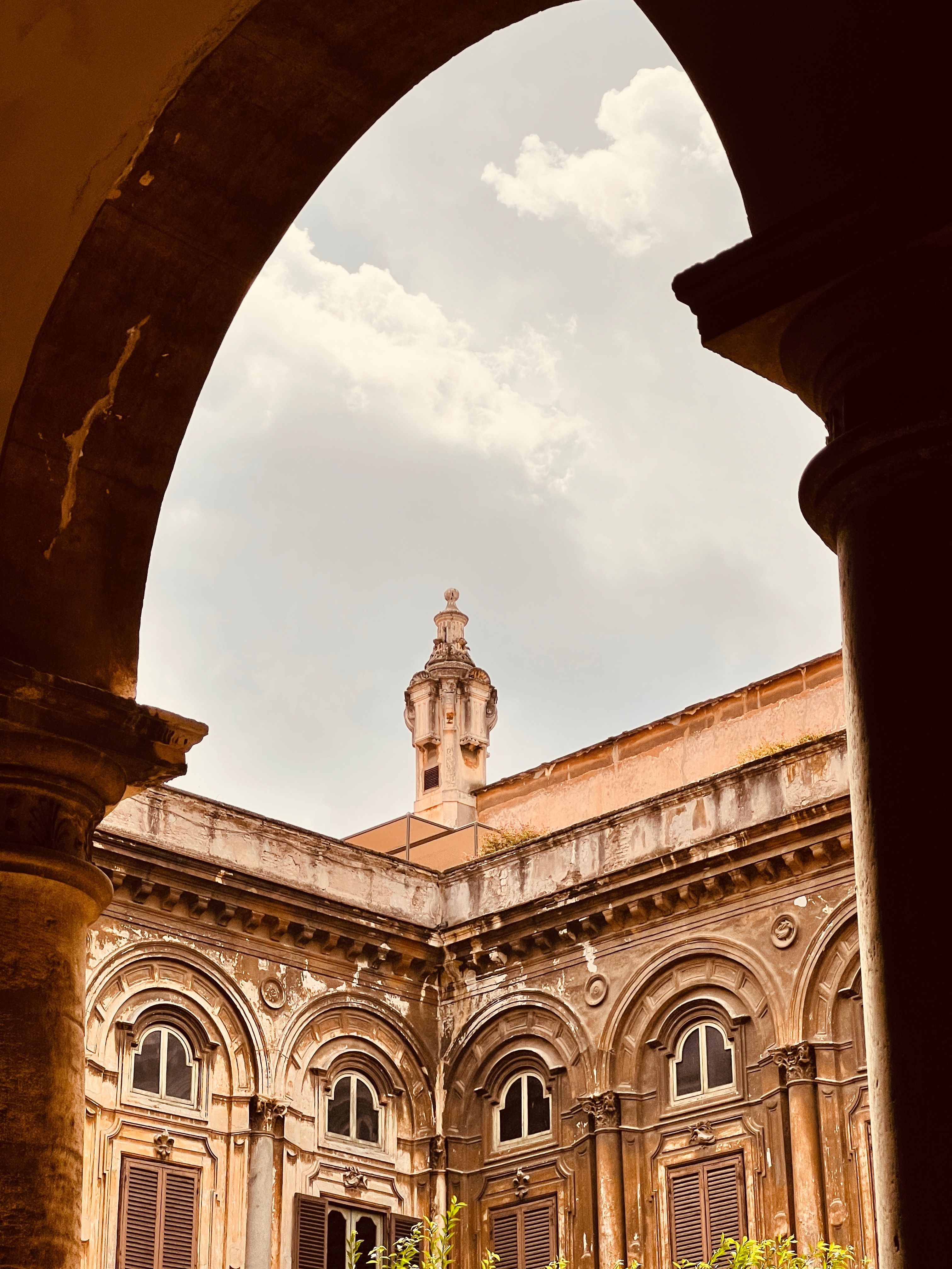 Elegant view of Italian historical architecture through a stone arch with cloudy sky backdrop.
