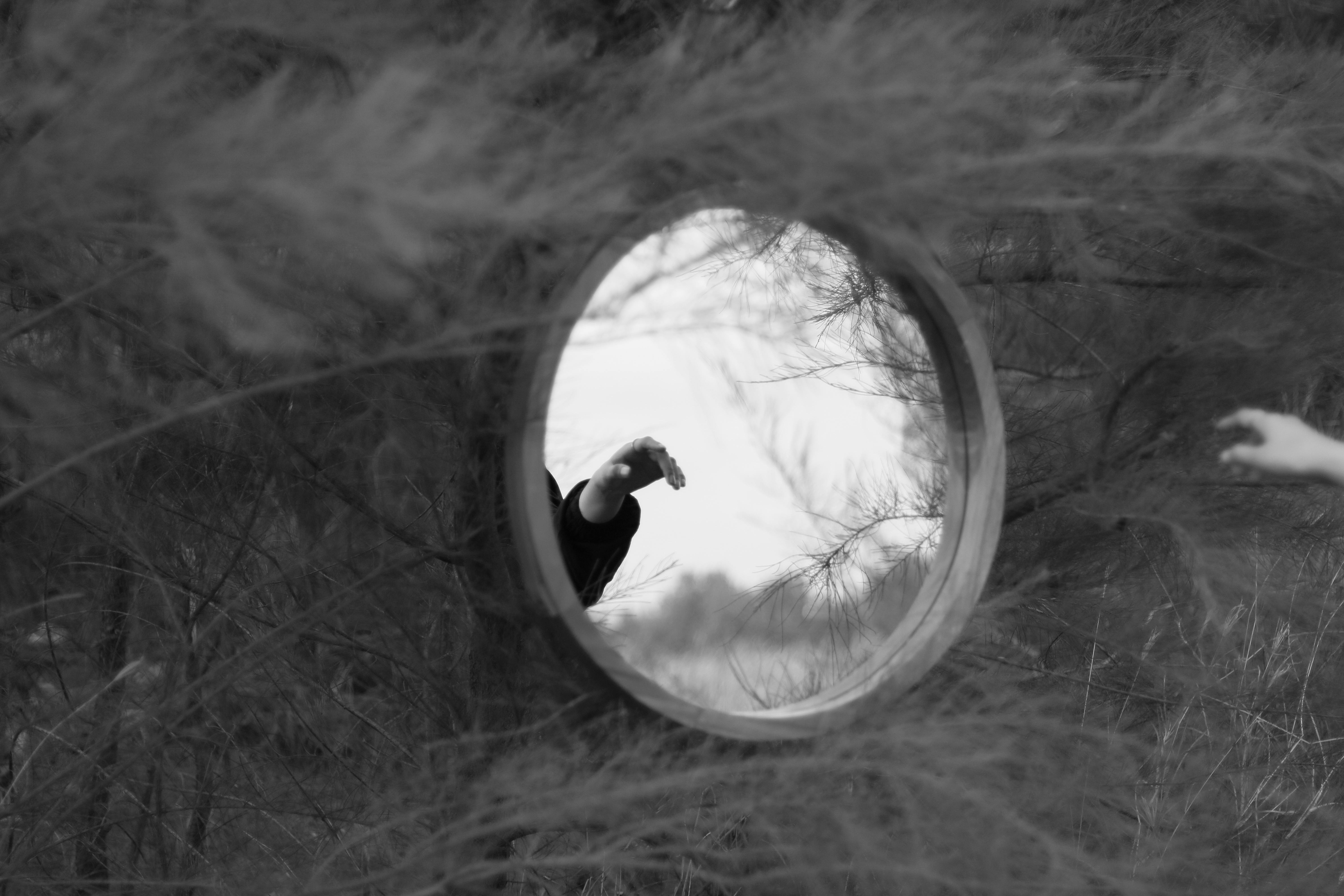 Creative black and white photo of a hand reflected in a circular mirror amidst nature.