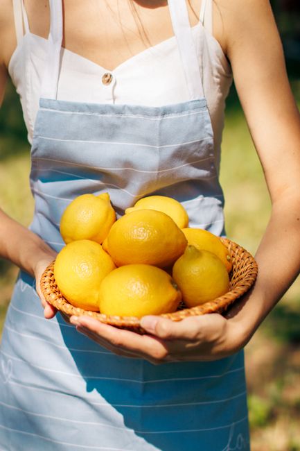 Close-up of a woman holding a wicker basket filled with fresh lemons outdoors on a sunny day.