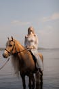 在日落之时，一名穿着白色裙子的女子正骑马漫步在湖边，周围一片宁静