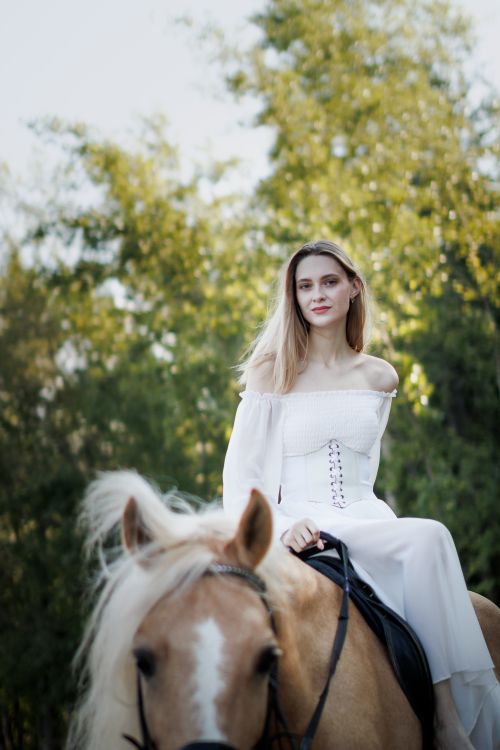 Free Woman in white dress sitting on a horse outdoors during the day. Stock Photo