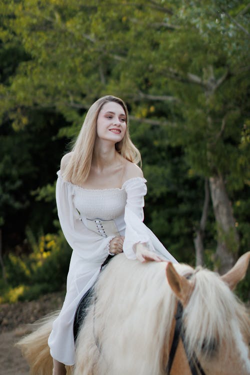 Smiling Woman in Long Sleeved Dress Touching Horse Mane