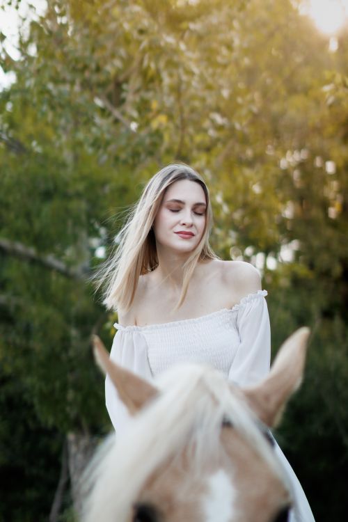 Free Woman in a white dress rides a horse in a serene rural landscape during the day. Stock Photo