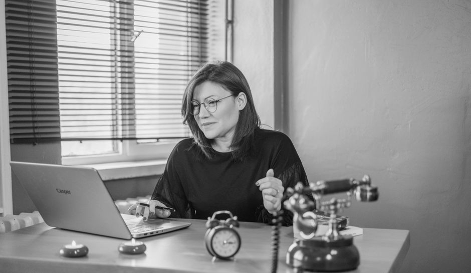 A businesswoman using a laptop at her desk with a vintage phone and an alarm clock, creating a mix of modern and retro vibes.