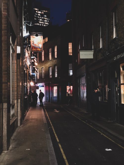 Free A city alley illuminated by soft lights, capturing the essence of nightlife with pedestrians. Stock Photo